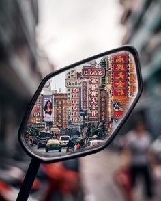 a rear view mirror on the side of a car with buildings in the background and people walking down the street