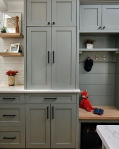 a kitchen with gray cabinets and white counter tops, including a red teddy bear sitting on the counter