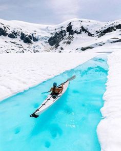 a person on a kayak in the middle of some water with mountains in the background