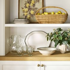 a shelf with plates, bowls and vases on it next to a basket full of lemons