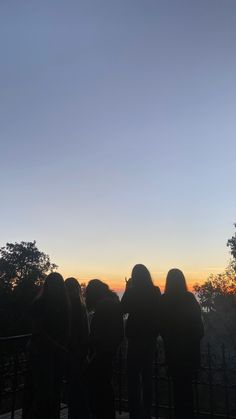 silhouettes of people looking at the sunset on a bridge over water with trees in the background