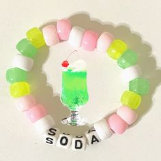 a green drink sitting on top of a white table next to candy beads with the word soda spelled in small letters