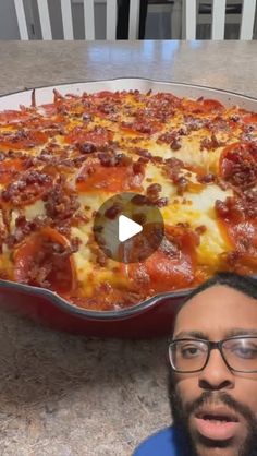 a man is standing in front of a large pan of cheese and pepperoni pizza