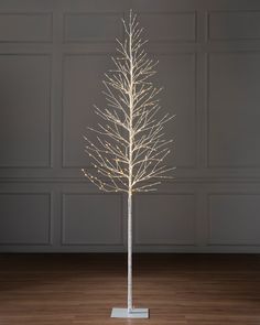 a white lighted tree in a room with wood flooring and gray wall behind it