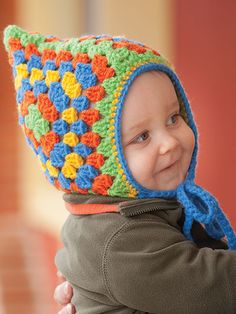 a young child wearing a crocheted hat and holding onto his father's arm