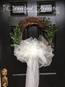 a wreath on the front door with a white bow hanging from it's side