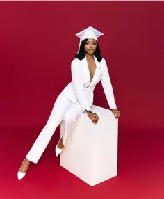 a woman in a white suit and cap sitting on top of a cubed box