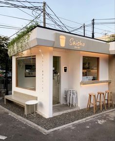 a small white building with some stools in front of it and an open window