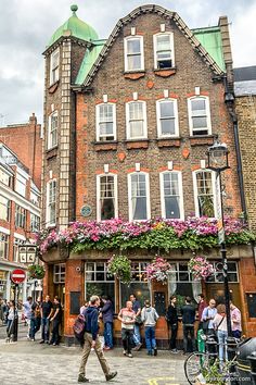 people are walking in front of a building with flowers growing on the roof and windows