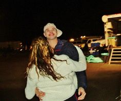 a man carrying a woman on his back in front of a bus at night time