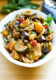 a white bowl filled with cooked vegetables on top of a wooden table next to a fork