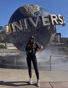 a woman standing in front of the universal studios sign with her hands on her hips