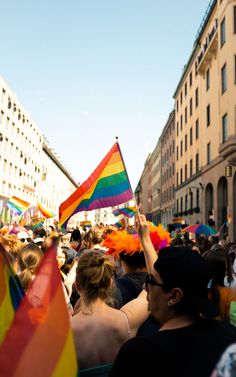 a group of people standing around each other holding rainbow colored flags and banners in their hands