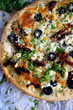 a pizza with olives, cheese and parsley on it sitting on wax paper