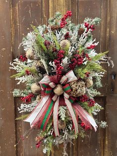 a christmas wreath with pine cones, berries and evergreens hanging on a wooden door