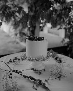 black and white photograph of a wedding cake with berries on the top, surrounded by greenery