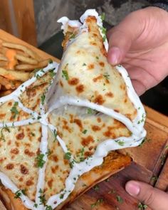 a person holding a slice of pizza with cheese and herbs on it, next to french fries