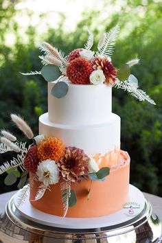 a three tiered wedding cake with flowers and foliage on top is sitting on a silver platter