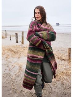 a woman is standing on the beach wearing a colorful coat