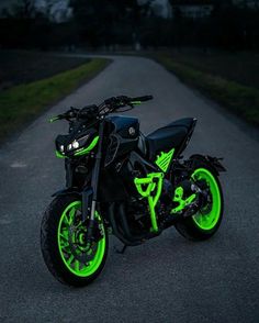 a black motorcycle with neon green wheels parked on the side of a road at night