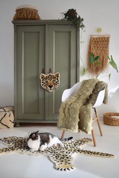 a black and white cat laying on top of a cheetah rug next to a green cabinet