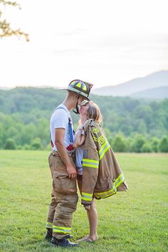 a man and woman dressed in firefighter gear standing on grass with mountains in the background