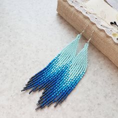 a pair of beaded earrings with blue beads hanging from the end of a piece of fabric