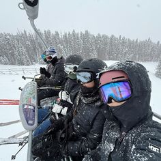 three people riding on a ski lift in the snow with goggles on their heads