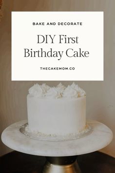 a white cake sitting on top of a table next to a sign that says, bake and decorate diy first birthday cake