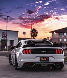 the rear end of a white sports car parked in front of a building at sunset