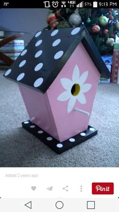 a pink birdhouse with polka dots and a flower painted on the side, sitting in front of a christmas tree