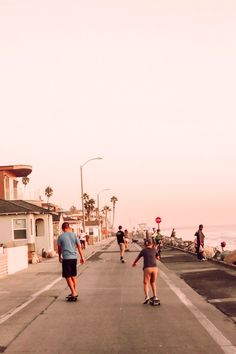 several people skateboarding down the street in front of some houses near the ocean with palm trees