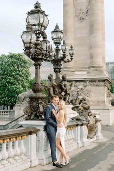 a man and woman standing next to each other in front of a light pole with lamps on it