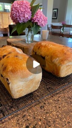 two loafs of bread sitting on top of a cooling rack next to a vase with flowers