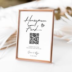 a white and gold frame with a qr code on it next to some feathers