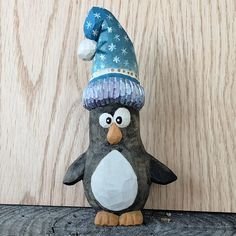 a stuffed penguin wearing a blue hat on top of a wooden table next to a wall