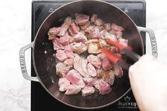 someone is cooking meat in a skillet on the stove with red spatulas