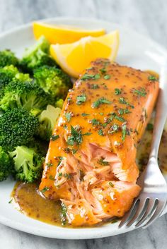 a white plate topped with salmon and broccoli next to lemon wedged potatoes