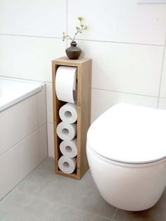 a white toilet sitting next to a wooden box with rolls of toilet paper in it