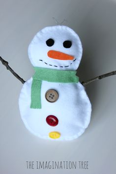 a white snowman with a green scarf and button on it's head, standing in front of a gray wall