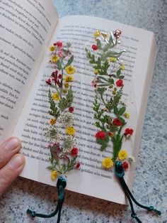 an open book with flowers on it and some string attached to the pages, sitting on a table