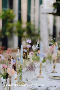 the table is set with white linens and colorful flowers in glass vases on each side