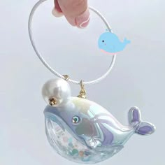 a hand holding a glass ornament with a blue whale on it's side