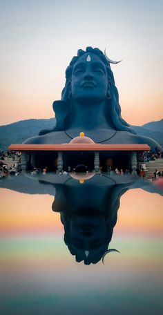 there is a large blue statue with its reflection in the water and people standing around it