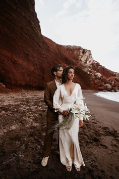 a man and woman standing on the beach next to each other holding flowers in their hands