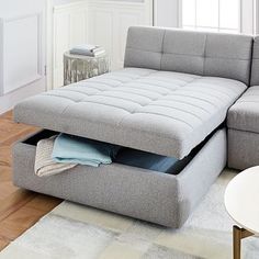 a grey couch with a pull out bed underneath it in a living room next to a coffee table