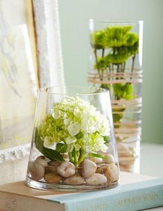 two vases filled with flowers and rocks on top of a table next to a book