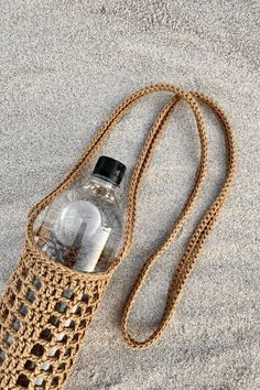 a water bottle in a crocheted bag on the sand with a chain attached to it