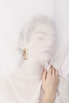 a woman is covering her face with a white sheet and wearing gold earrings