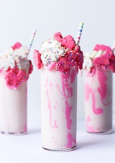 three milkshakes with sprinkles and toppings in glass cups on white surface